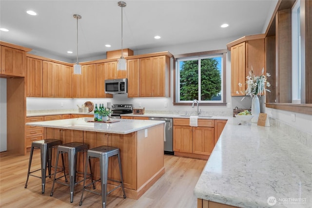 kitchen featuring appliances with stainless steel finishes, light stone counters, a kitchen bar, a sink, and recessed lighting