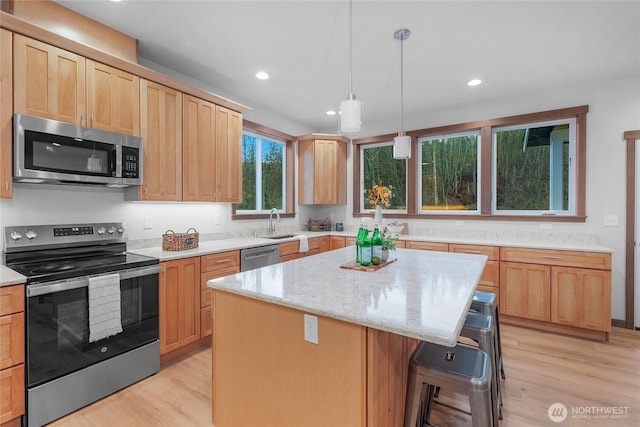 kitchen featuring appliances with stainless steel finishes, a kitchen island, light stone counters, and light wood-style floors