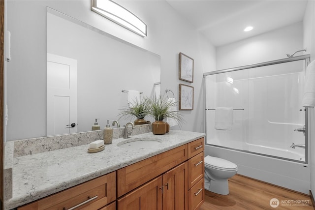 bathroom featuring toilet, combined bath / shower with glass door, wood finished floors, and vanity