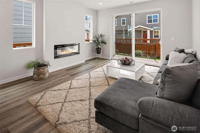 living area with wood finished floors, recessed lighting, a glass covered fireplace, and baseboards