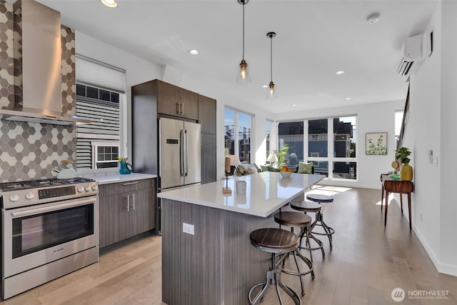 kitchen with stainless steel appliances, backsplash, an AC wall unit, wall chimney range hood, and a kitchen breakfast bar