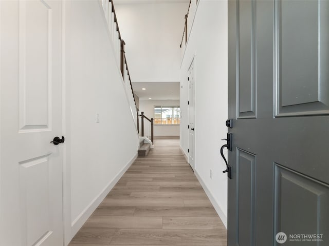 hallway with light wood-type flooring, baseboards, and stairs