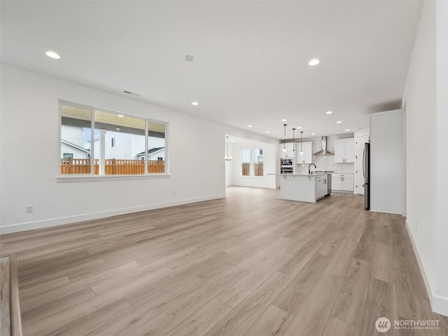 unfurnished living room featuring light wood-style flooring, recessed lighting, a sink, visible vents, and baseboards