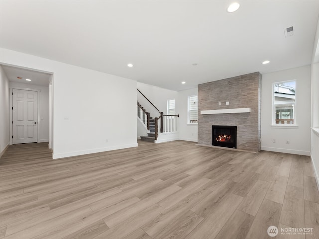 unfurnished living room featuring light wood finished floors, plenty of natural light, stairway, and a large fireplace