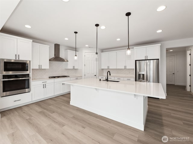 kitchen featuring light countertops, appliances with stainless steel finishes, an island with sink, and wall chimney range hood