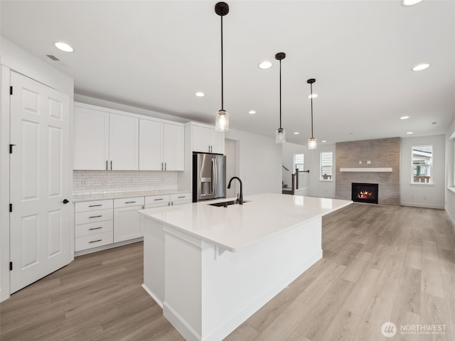 kitchen featuring a sink, white cabinets, light countertops, stainless steel fridge, and pendant lighting