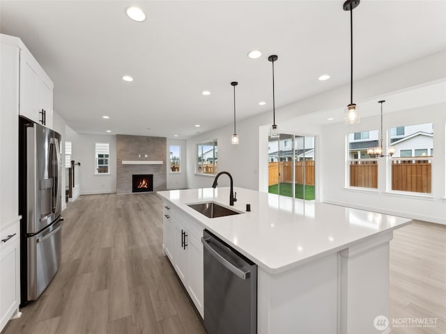 kitchen featuring an island with sink, appliances with stainless steel finishes, hanging light fixtures, light countertops, and a sink