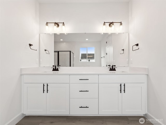 full bathroom with double vanity, a stall shower, baseboards, and a sink