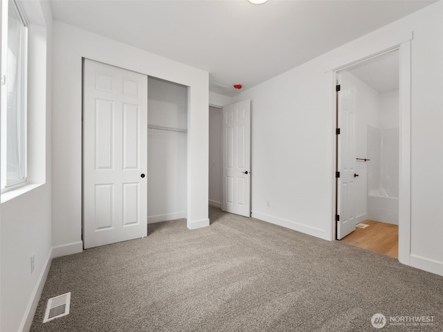 unfurnished bedroom with light carpet, a closet, ensuite bath, and visible vents