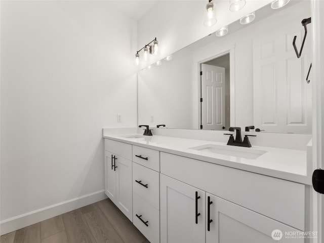 bathroom with double vanity, baseboards, a sink, and wood finished floors