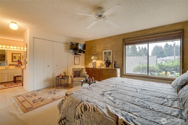 bedroom with a ceiling fan, light colored carpet, ensuite bath, a textured ceiling, and a closet