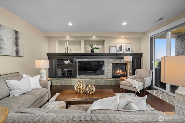 living room with recessed lighting, visible vents, a stone fireplace, and wood finished floors