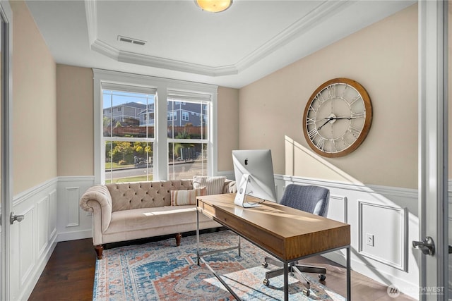 office featuring a tray ceiling, visible vents, ornamental molding, wainscoting, and wood finished floors