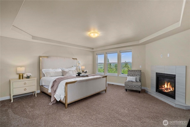 carpeted bedroom with baseboards, a tray ceiling, and a tiled fireplace