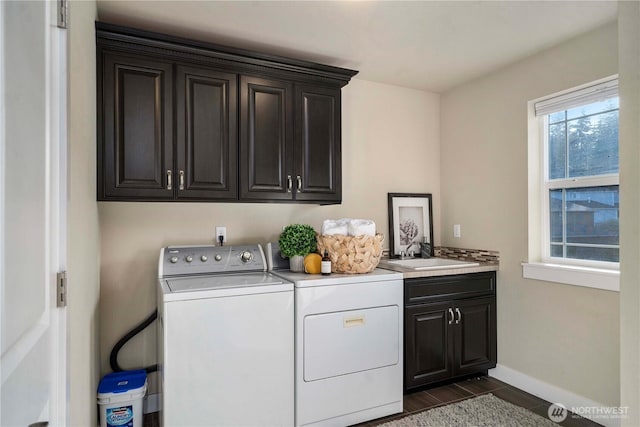 clothes washing area featuring dark wood-type flooring, a sink, baseboards, independent washer and dryer, and cabinet space