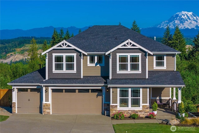 craftsman-style home with a mountain view, a garage, stone siding, driveway, and roof with shingles