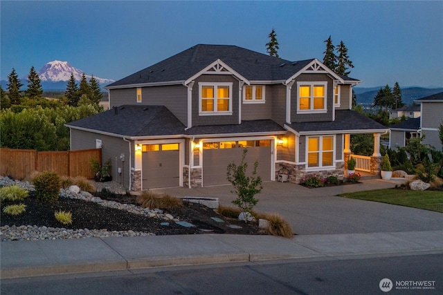 craftsman-style home with a garage, stone siding, fence, and a mountain view