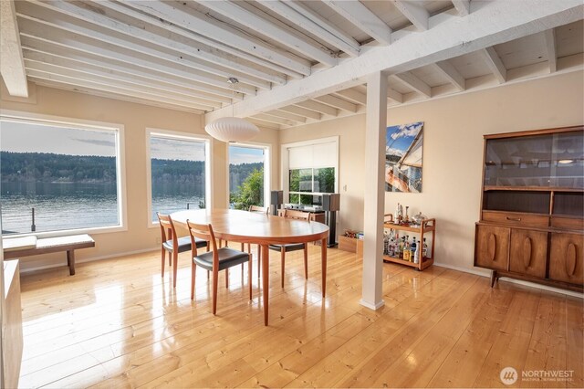 dining area featuring light wood-style floors, a water view, beamed ceiling, and baseboards