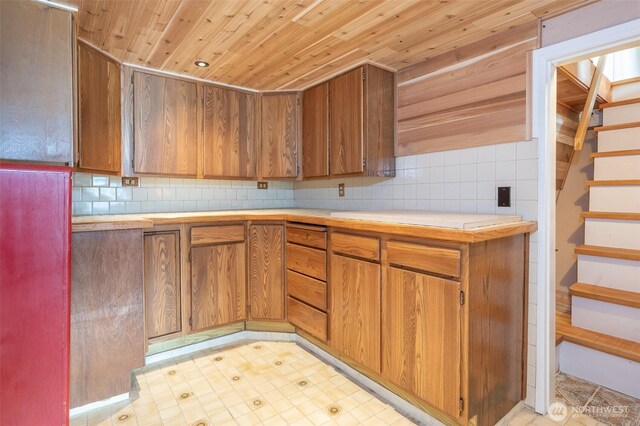 kitchen featuring light floors, tasteful backsplash, light countertops, brown cabinetry, and wooden ceiling