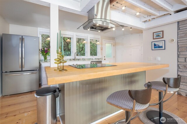 interior space with island range hood, butcher block countertops, freestanding refrigerator, light wood-style floors, and a kitchen bar