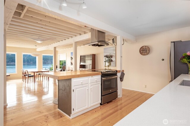 kitchen featuring stainless steel appliances, light wood-style floors, white cabinets, wooden counters, and wall chimney exhaust hood