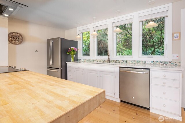 kitchen featuring light wood finished floors, appliances with stainless steel finishes, white cabinetry, pendant lighting, and a sink