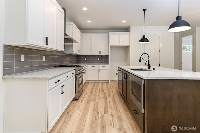 kitchen featuring stainless steel appliances, exhaust hood, a sink, white cabinetry, and pendant lighting