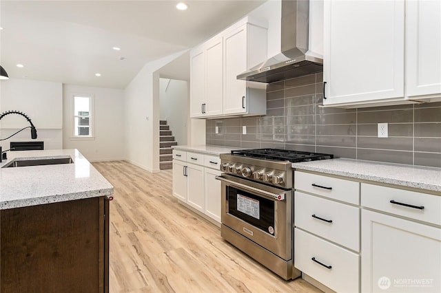 kitchen featuring stainless steel gas stove, wall chimney exhaust hood, a sink, and white cabinetry