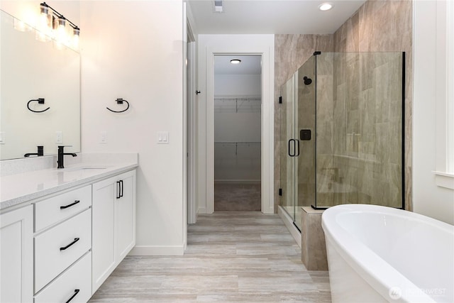 bathroom featuring a freestanding tub, vanity, baseboards, a spacious closet, and a stall shower