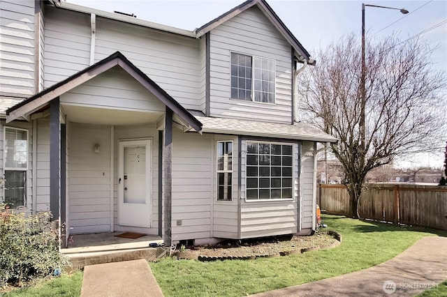 view of front of home with a front yard, roof with shingles, and fence