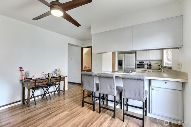 kitchen featuring a breakfast bar area, light wood finished floors, appliances with stainless steel finishes, a sink, and a peninsula