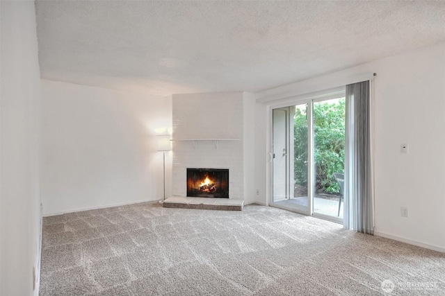 unfurnished living room with a textured ceiling, a brick fireplace, carpet flooring, and baseboards