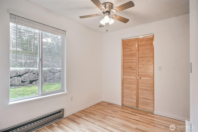 unfurnished bedroom featuring a textured ceiling, a baseboard radiator, baseboards, a closet, and light wood-type flooring