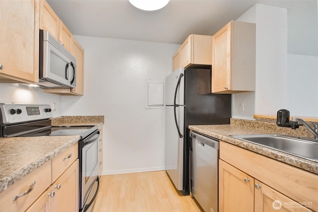 kitchen featuring light wood finished floors, stainless steel appliances, light countertops, light brown cabinets, and a sink