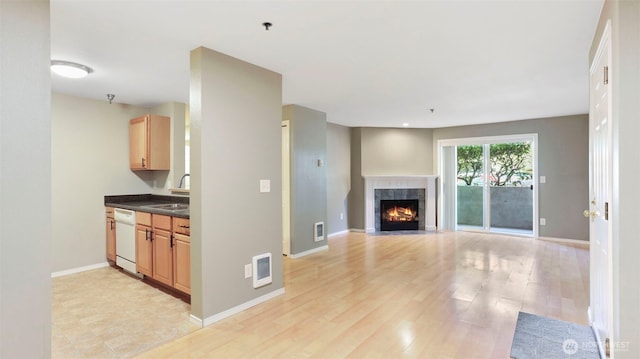 unfurnished living room with visible vents, light wood-style flooring, a fireplace with flush hearth, a sink, and baseboards