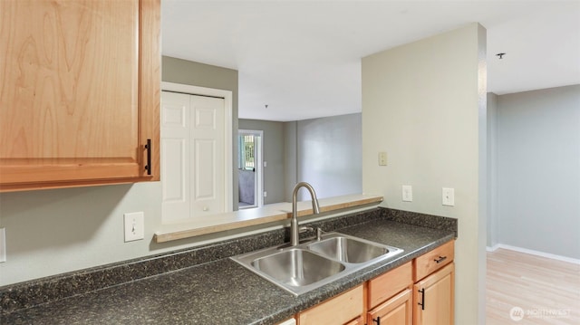 kitchen featuring light wood-type flooring, a sink, baseboards, and light brown cabinetry