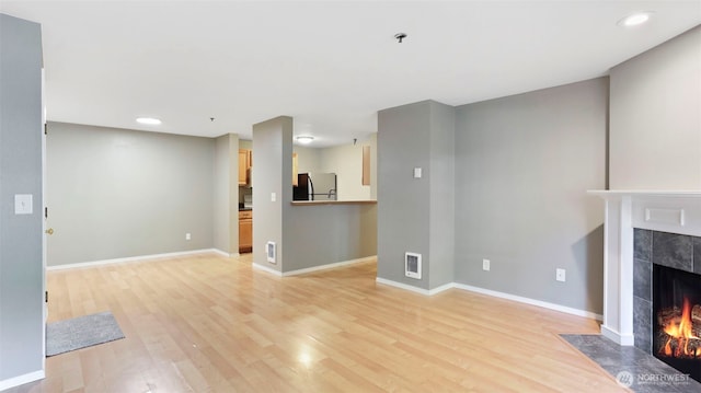 unfurnished living room with light wood-style flooring, a tiled fireplace, visible vents, and baseboards