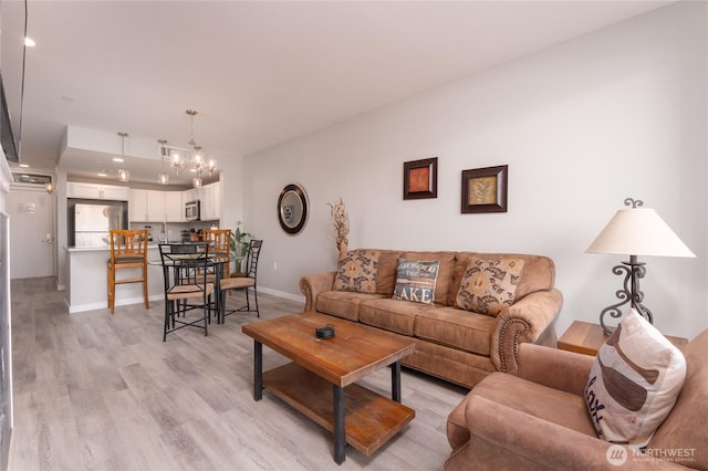 living area featuring light wood finished floors, baseboards, and an inviting chandelier