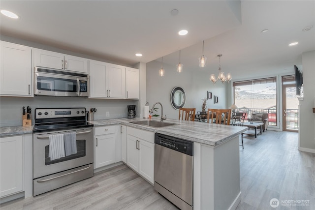 kitchen with white cabinets, appliances with stainless steel finishes, a peninsula, light wood-type flooring, and a sink