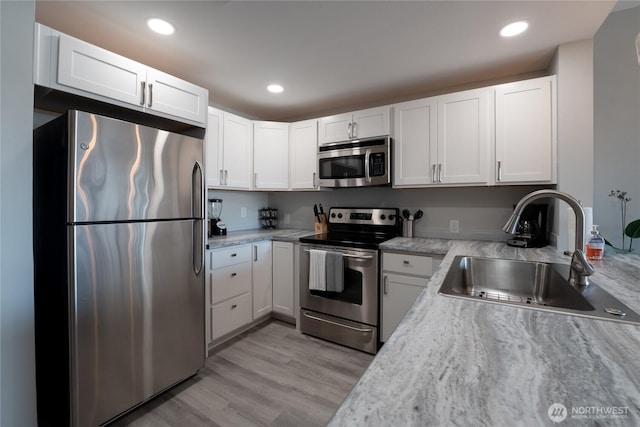 kitchen featuring recessed lighting, stainless steel appliances, a sink, white cabinetry, and light wood finished floors