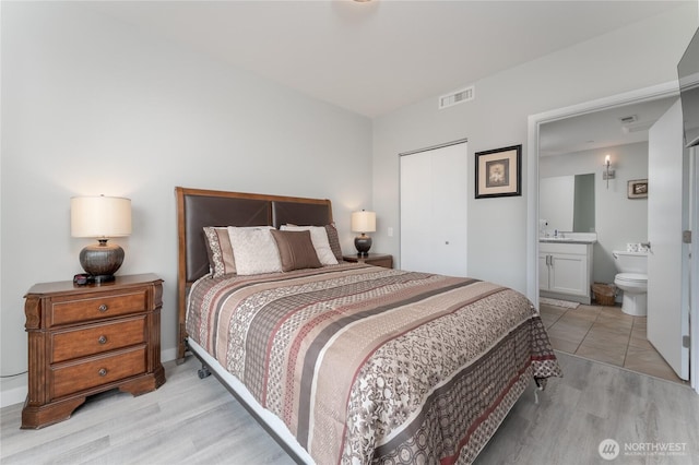 bedroom featuring ensuite bathroom, a sink, visible vents, a closet, and light wood-type flooring