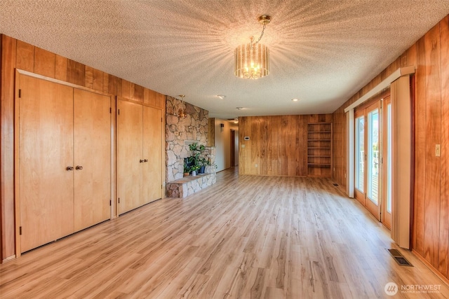 interior space featuring a textured ceiling, a stone fireplace, wooden walls, visible vents, and light wood finished floors