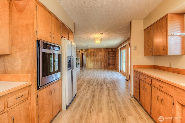 kitchen with light countertops, white refrigerator with ice dispenser, oven, and a textured ceiling