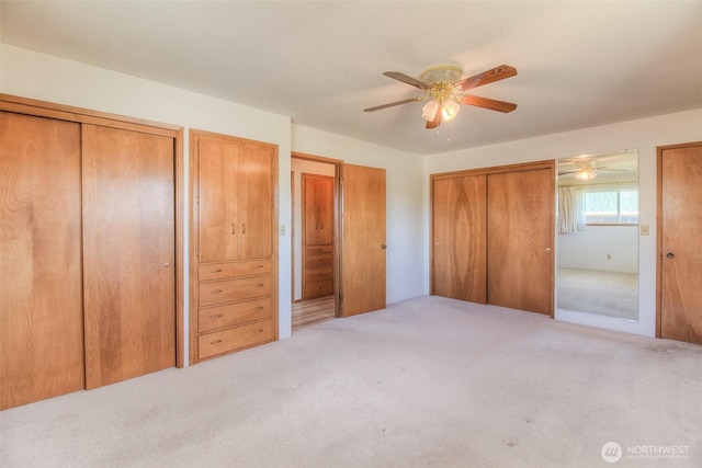 unfurnished bedroom with multiple closets, carpet flooring, and ceiling fan