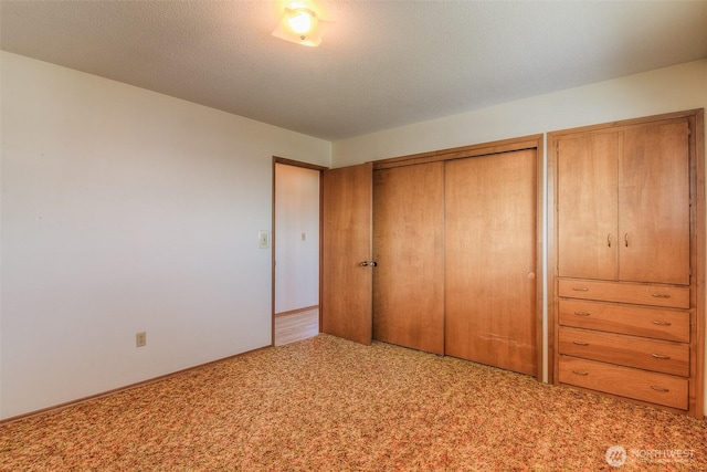 unfurnished bedroom with a textured ceiling, carpet floors, and a closet