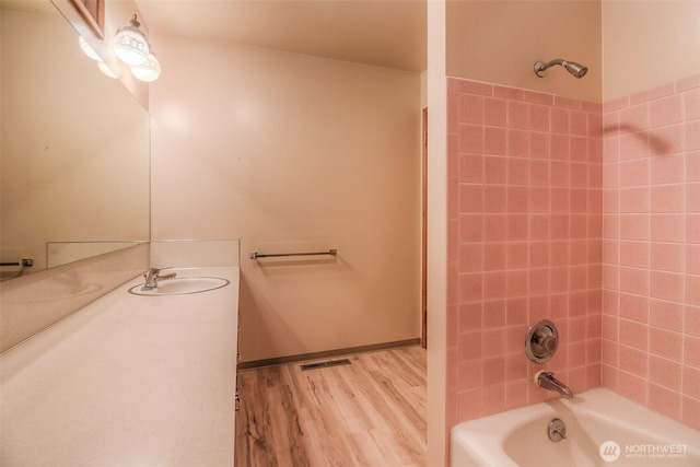 full bath featuring wood finished floors, vanity, visible vents, baseboards, and tub / shower combination