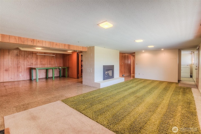 unfurnished living room with wooden walls, washer / clothes dryer, a fireplace with raised hearth, and a textured ceiling