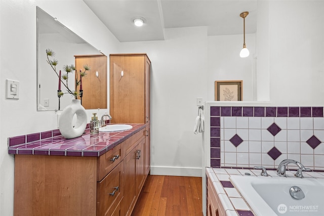 bathroom featuring tiled bath, tasteful backsplash, baseboards, wood finished floors, and vanity