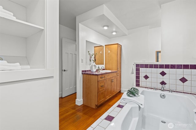 bathroom featuring a garden tub, vanity, baseboards, and wood finished floors