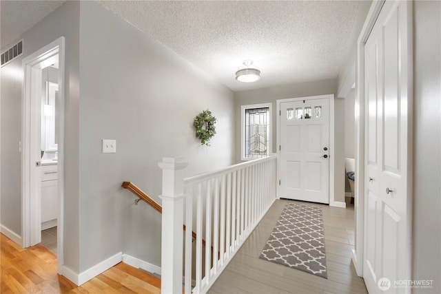 entrance foyer featuring baseboards, light wood-style floors, visible vents, and a textured ceiling